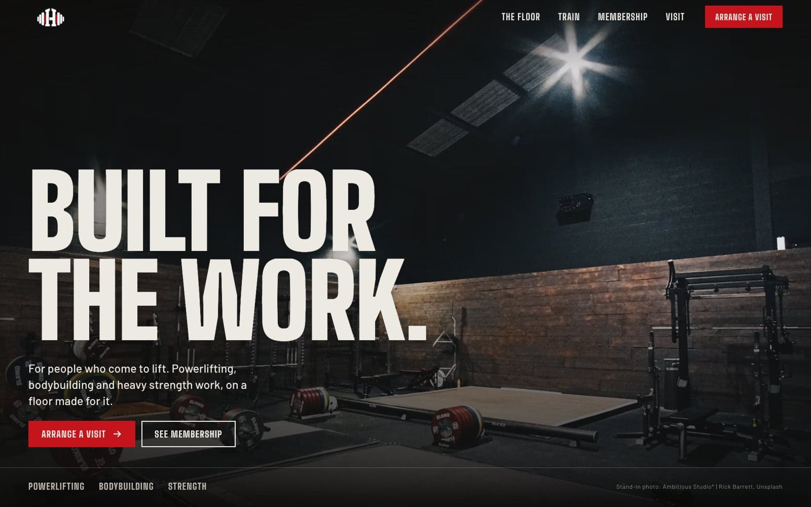 IRON HOUSE homepage: “Built for the work.” in heavy condensed capitals over a dark gym with spotlit lifting platforms and loaded barbells